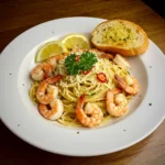 Garlic shrimp pasta recipe topped with grated cheese, parsley, and served with garlic bread and lemon slice.