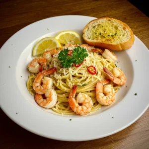 Garlic shrimp pasta recipe topped with grated cheese, parsley, and served with garlic bread and lemon slice.