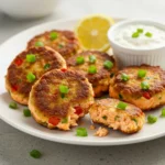 Golden-brown salmon cakes recipe garnished with green onions and served with lemon slices and a creamy dipping sauce.